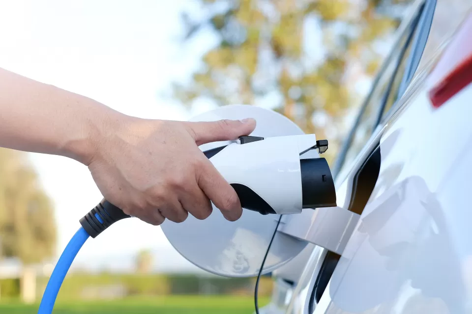 Close-up of hand holding charging cable moving toward charging port on electric car.